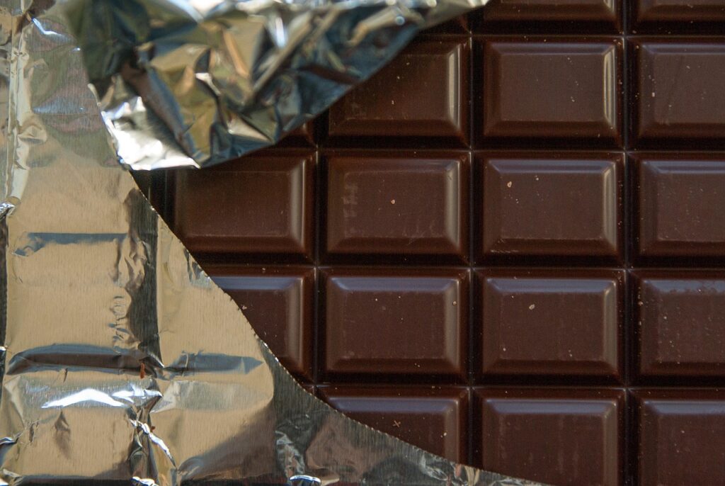 Pieces of dark chocolate on a wooden plate with berries and nuts